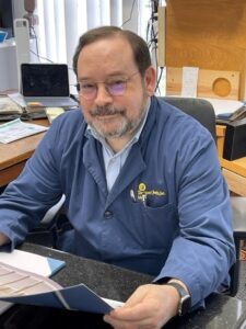 Man in blue coat sitting at desk.