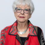 Elderly woman with white hair and glasses wearing a red patterned shawl.