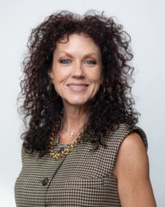 Smiling woman with curly hair and a sleeveless checkered top.